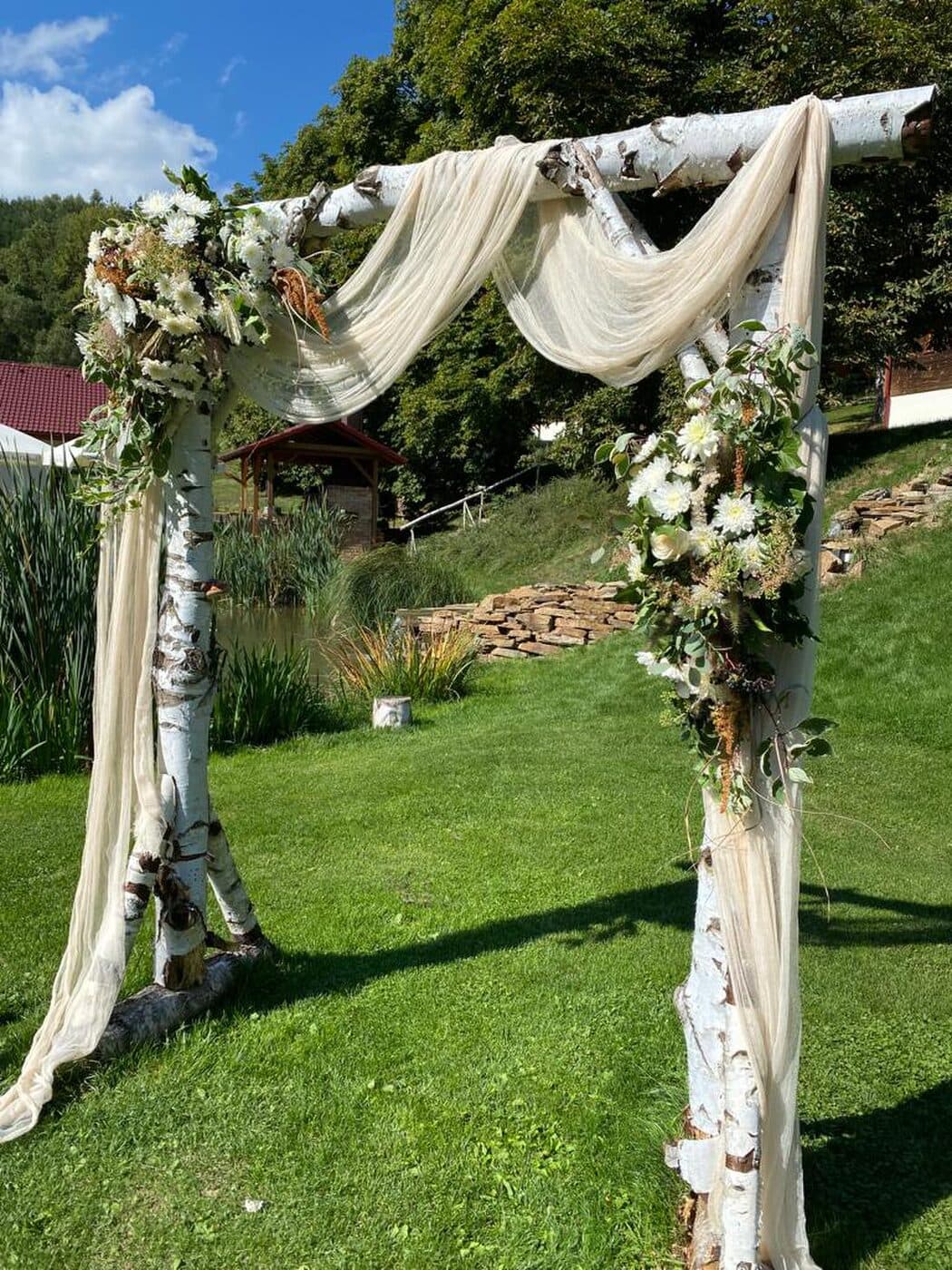 Hochzeitsbogen mit weißen Stoffen und Blumen